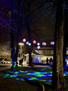 Nightime photo, with glowing orbs hanging from a tree and green and blue lights illuminating the grass below. 